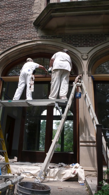 Two men painting a window with white paint.