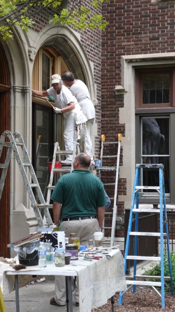 Three men are painting a house with ladders.