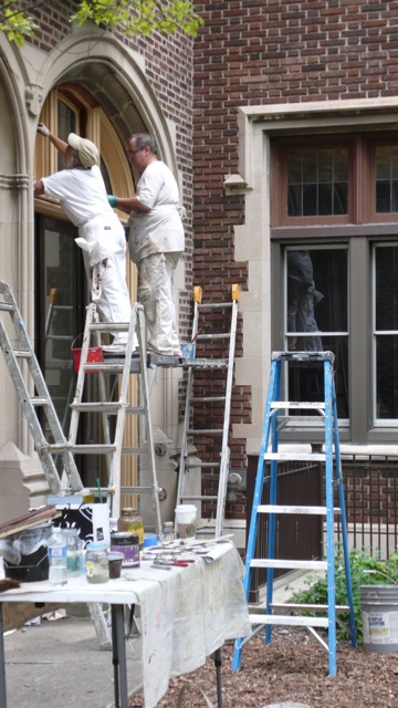 Two men painting a building with ladders and paint.